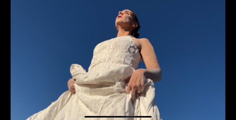 Rosely Conz wearing a white dress picking up the side of the dress and looking up the sky